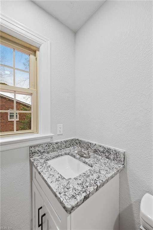 bathroom featuring toilet, vanity, and a textured wall