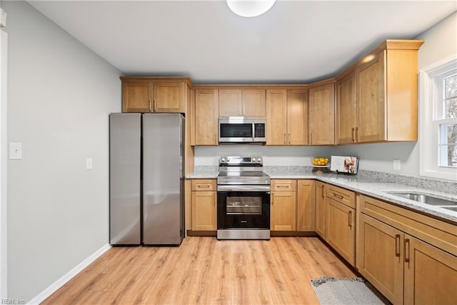 kitchen featuring baseboards, light stone counters, light wood-style flooring, appliances with stainless steel finishes, and a sink