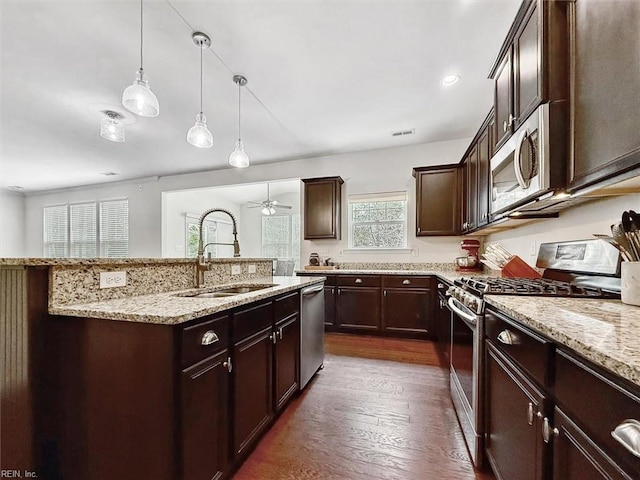 kitchen with a sink, stainless steel appliances, light stone counters, and dark brown cabinetry