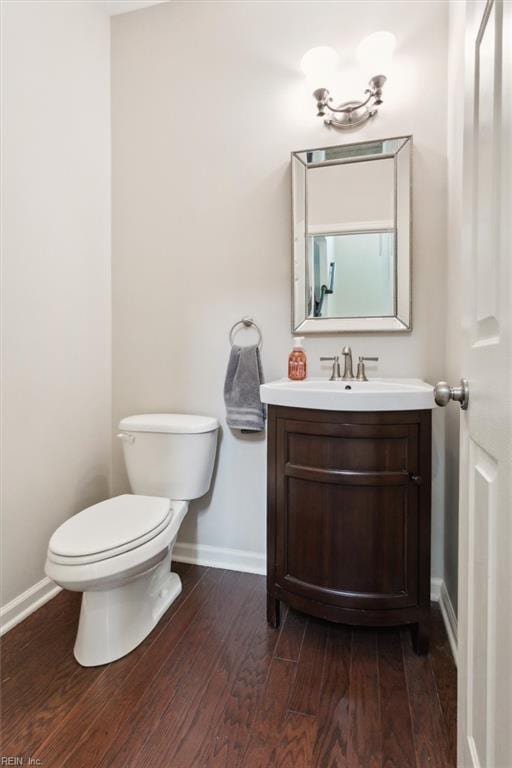 half bathroom featuring vanity, toilet, wood finished floors, and baseboards