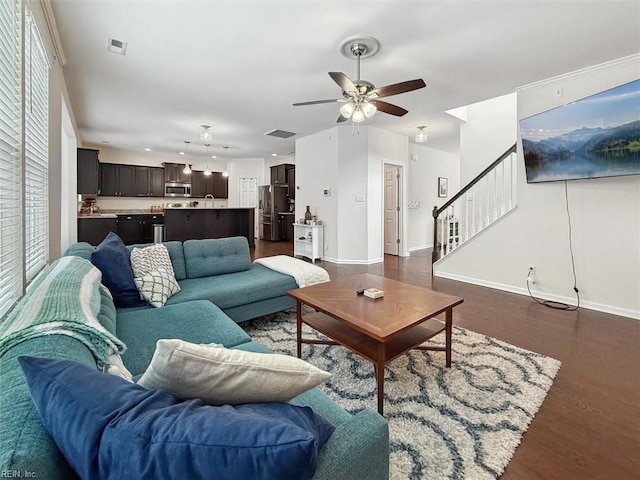 living room with stairs, visible vents, a ceiling fan, and dark wood-style flooring