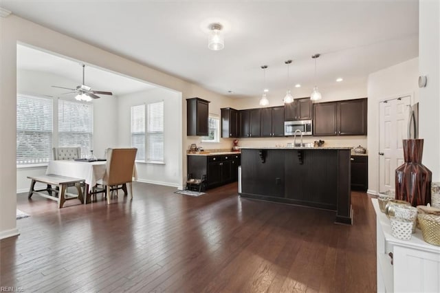 kitchen with a ceiling fan, dark wood-style floors, a breakfast bar, dark brown cabinetry, and stainless steel microwave