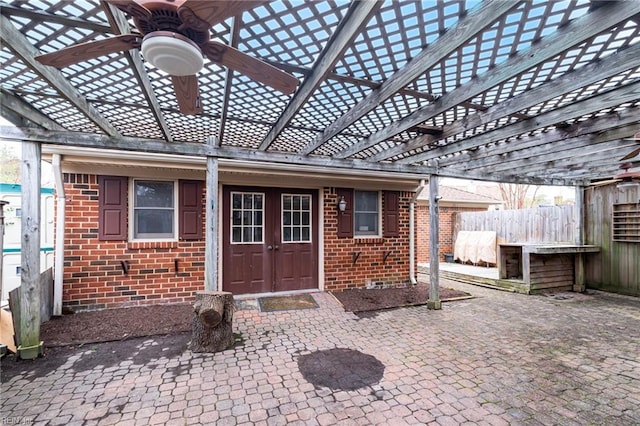 view of exterior entry with a pergola, fence, crawl space, brick siding, and ceiling fan