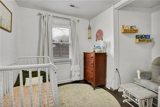 bedroom featuring visible vents, a crib, baseboards, and wood finished floors