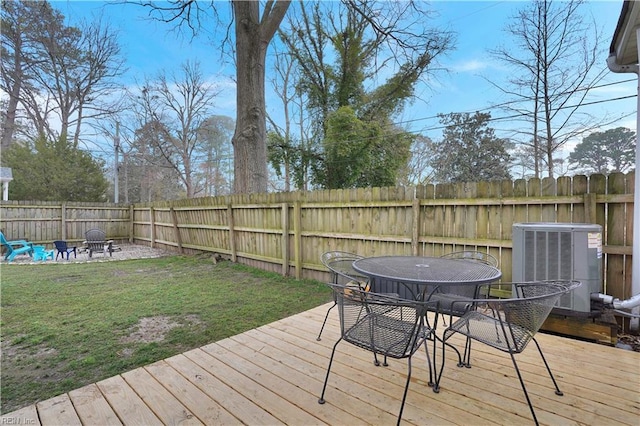 wooden terrace featuring outdoor dining space, central AC unit, an outdoor fire pit, a fenced backyard, and a lawn