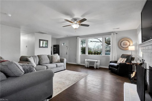 living room featuring a ceiling fan, visible vents, baseboards, a fireplace, and dark wood-style flooring