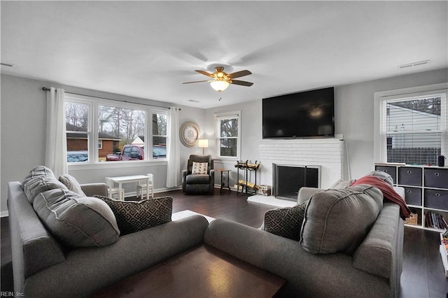 living area with dark wood finished floors, a ceiling fan, a wealth of natural light, and a fireplace