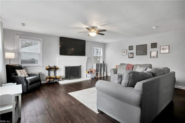 living room with a fireplace with raised hearth, dark wood-style floors, visible vents, and ceiling fan