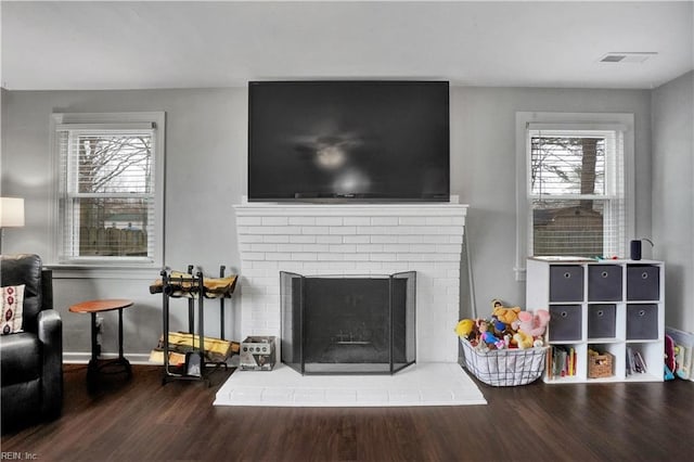 living area featuring visible vents, plenty of natural light, a brick fireplace, and wood finished floors