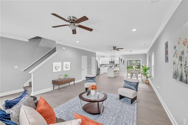 living area featuring stairs, crown molding, baseboards, and ceiling fan