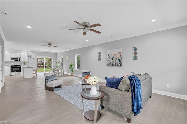 living area with crown molding, a ceiling fan, and baseboards