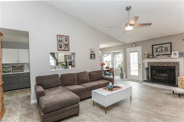 living room featuring a toaster, high vaulted ceiling, a ceiling fan, and a tile fireplace