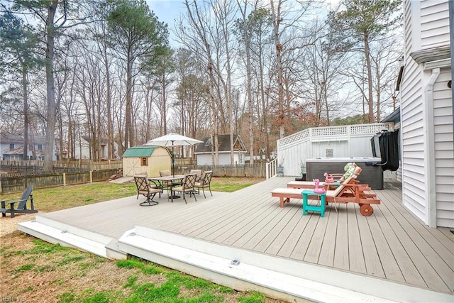 deck with a storage unit, outdoor dining space, a fenced backyard, an outdoor structure, and a hot tub