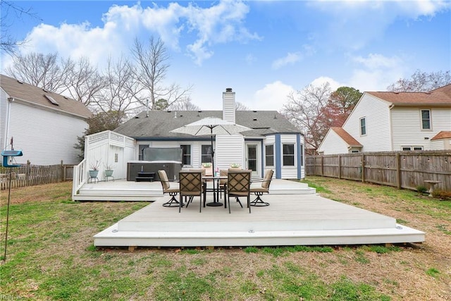 back of house featuring a deck, a fenced backyard, a yard, a chimney, and a hot tub