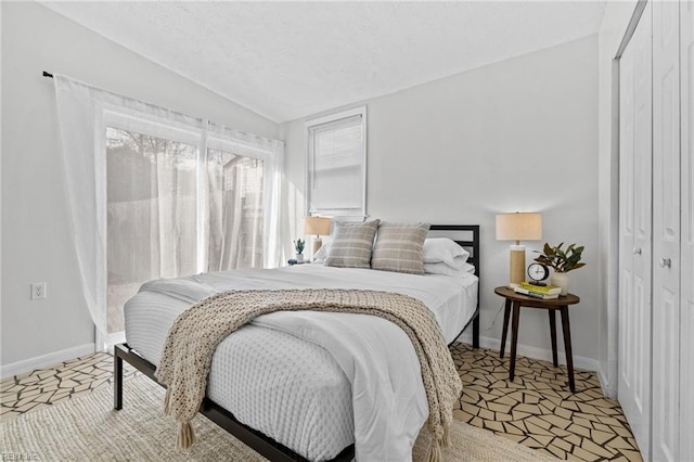 bedroom featuring a closet, a textured ceiling, baseboards, and vaulted ceiling