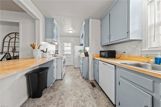 kitchen featuring white appliances, gray cabinetry, a sink, backsplash, and butcher block counters