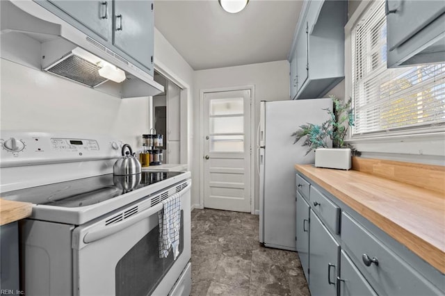 kitchen featuring gray cabinetry, under cabinet range hood, butcher block counters, stone finish floor, and white appliances