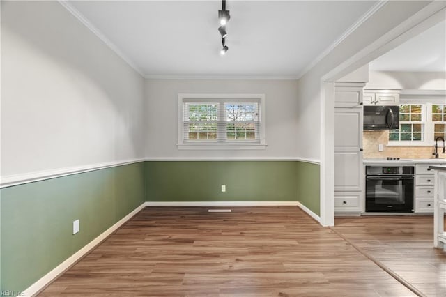 unfurnished dining area featuring baseboards, ornamental molding, and light wood finished floors