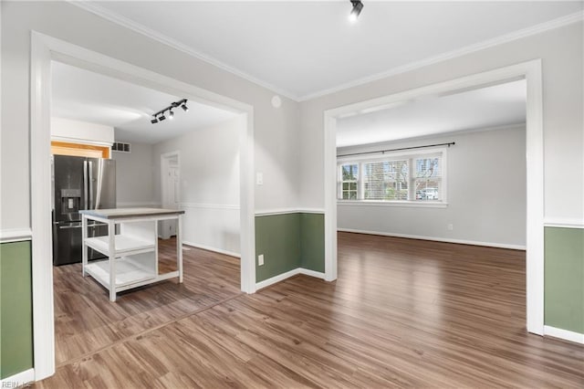 empty room with visible vents, track lighting, wood finished floors, crown molding, and baseboards