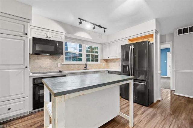 kitchen with tasteful backsplash, visible vents, black appliances, wood finished floors, and white cabinetry