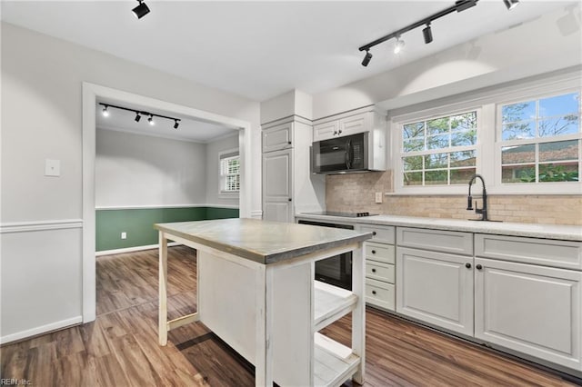 kitchen with black appliances, a sink, dark wood-style floors, light countertops, and decorative backsplash