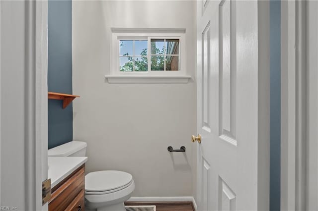 half bath featuring vanity, toilet, baseboards, and visible vents