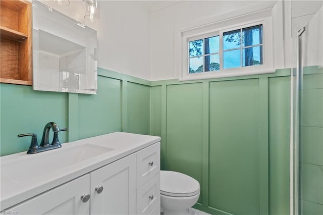 full bath with toilet, wainscoting, a shower with shower door, a decorative wall, and vanity