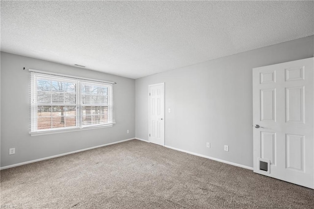 spare room with baseboards, carpet floors, a textured ceiling, and visible vents