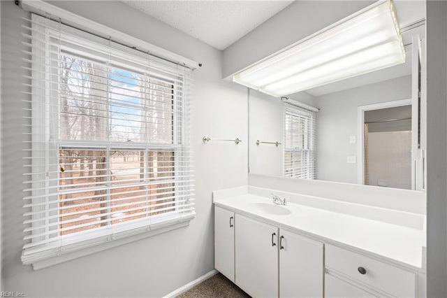 bathroom featuring baseboards, a textured ceiling, a healthy amount of sunlight, and vanity