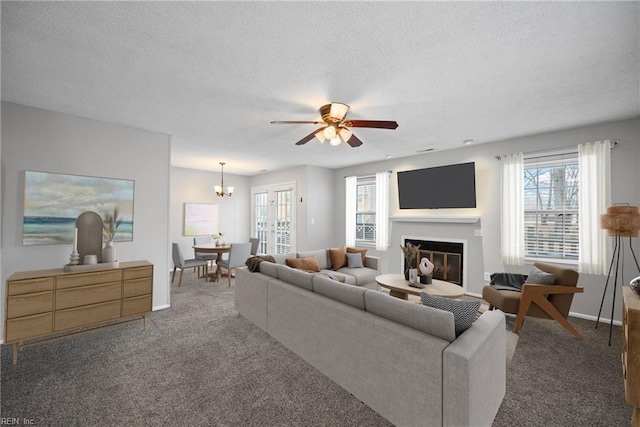 carpeted living room with a glass covered fireplace, ceiling fan with notable chandelier, baseboards, and a textured ceiling