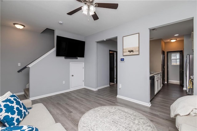 living room featuring stairway, baseboards, wood finished floors, and a ceiling fan