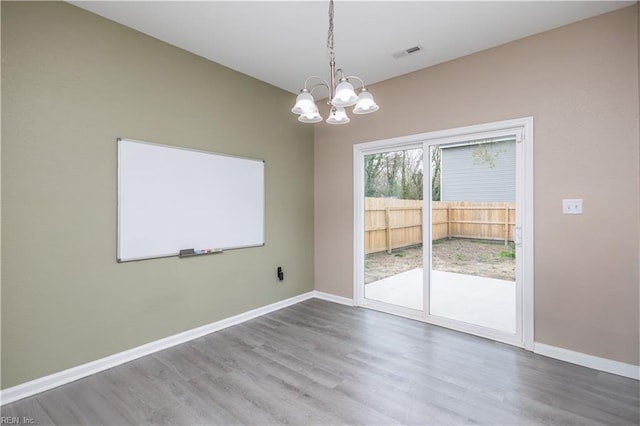 spare room featuring visible vents, baseboards, an inviting chandelier, and wood finished floors