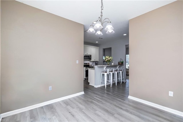 unfurnished dining area featuring light wood finished floors, a notable chandelier, and baseboards