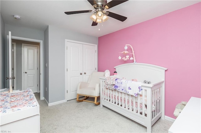 bedroom featuring a ceiling fan, baseboards, carpet floors, a crib, and a closet