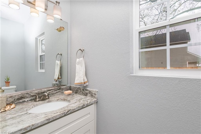 half bathroom featuring toilet, vanity, and a textured wall