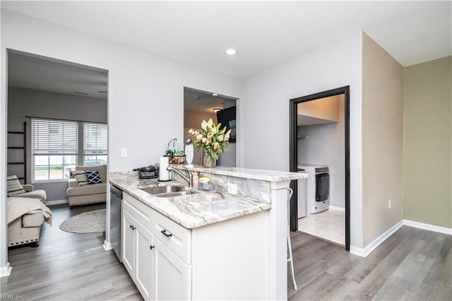 kitchen featuring light stone countertops, light wood finished floors, washer / clothes dryer, a sink, and white cabinets