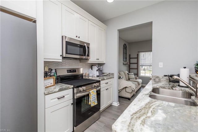 kitchen featuring light wood-style flooring, a sink, decorative backsplash, appliances with stainless steel finishes, and white cabinetry