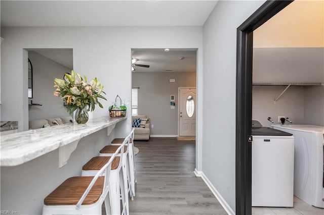 corridor with washing machine and clothes dryer, baseboards, and light wood-style floors