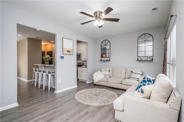 living area featuring visible vents, baseboards, ceiling fan, and wood finished floors