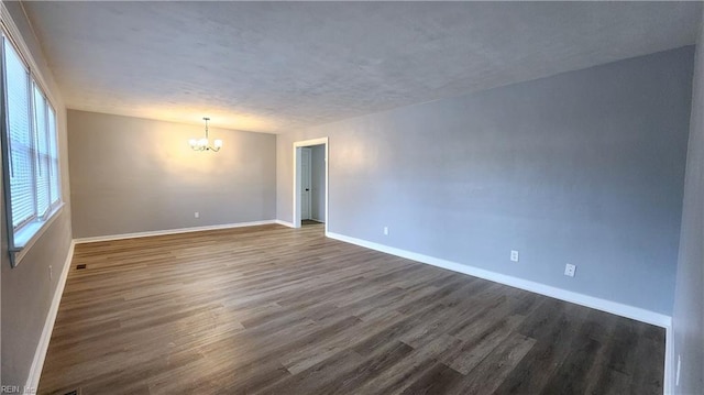 spare room featuring a textured ceiling, dark wood-style floors, baseboards, and a chandelier