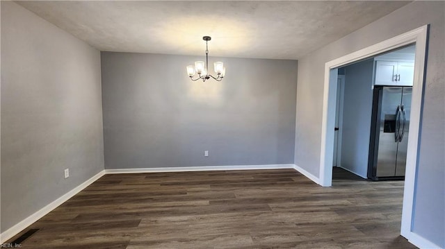 spare room featuring dark wood finished floors, visible vents, baseboards, and a chandelier