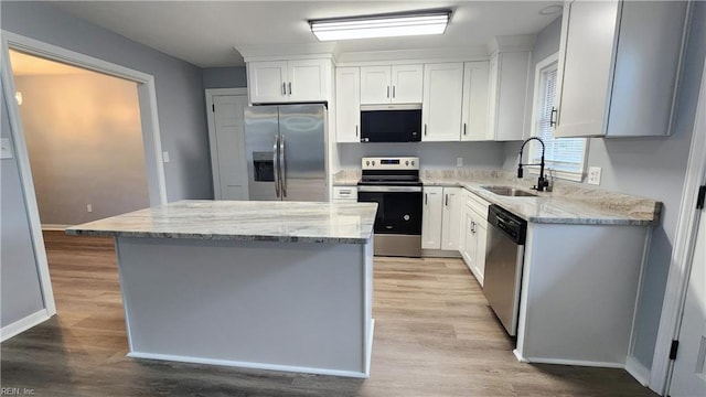 kitchen featuring light stone counters, appliances with stainless steel finishes, a kitchen island, and a sink