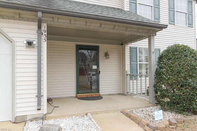 entrance to property featuring a porch and roof with shingles