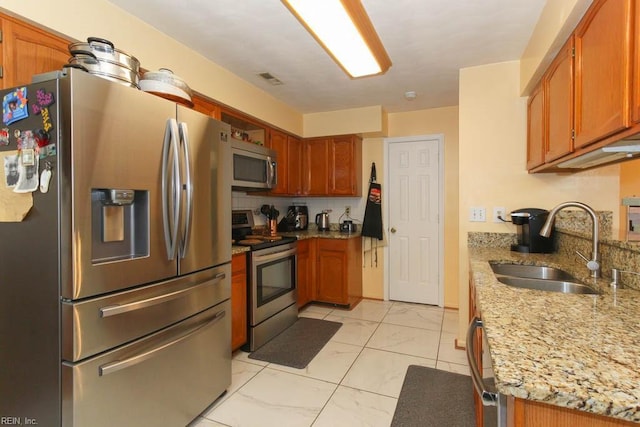 kitchen featuring light stone counters, a sink, stainless steel appliances, marble finish floor, and backsplash