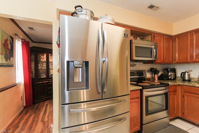 kitchen with decorative backsplash, visible vents, appliances with stainless steel finishes, and brown cabinets