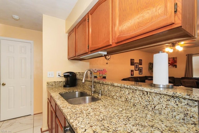 kitchen with brown cabinetry, marble finish floor, light stone countertops, and a sink