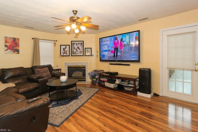 living room featuring a glass covered fireplace, visible vents, ceiling fan, and wood finished floors