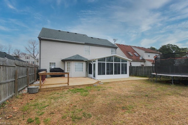 rear view of house with a deck, a trampoline, a fenced backyard, a yard, and a sunroom