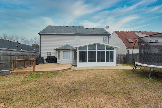 back of property featuring a fenced backyard, a sunroom, a deck, a trampoline, and a lawn