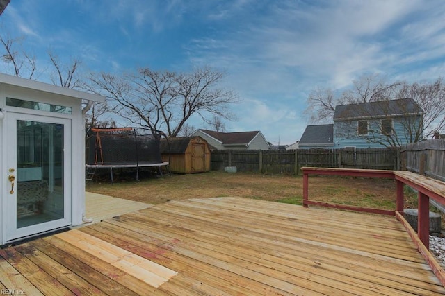 wooden terrace featuring a trampoline, a shed, a lawn, a fenced backyard, and an outbuilding